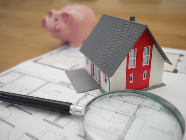 small red and white house next to a pink pig and magnifying glass