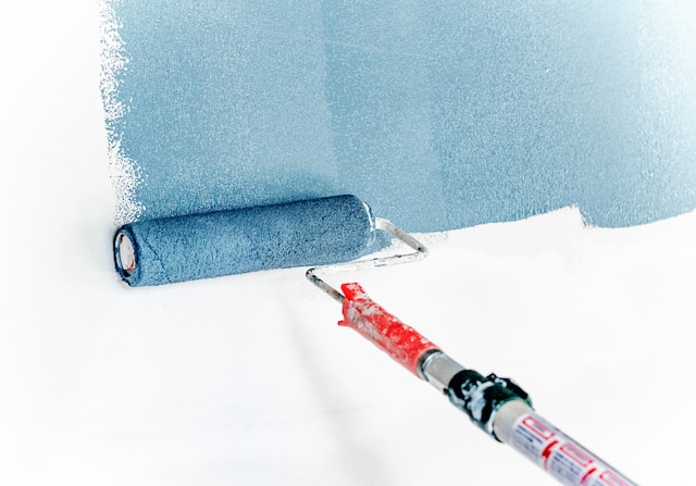 White wall being painted with blue paint using a paint roller